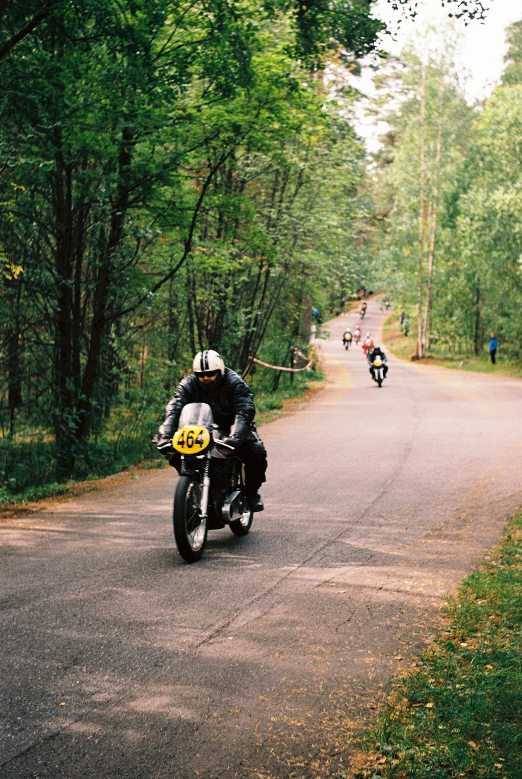 A person driving a motorcycle on a road with a forest background.
