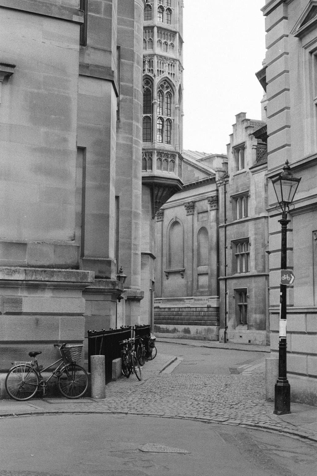 A street lamp and a bycicle in the foreground with a city street and buildings on the background.