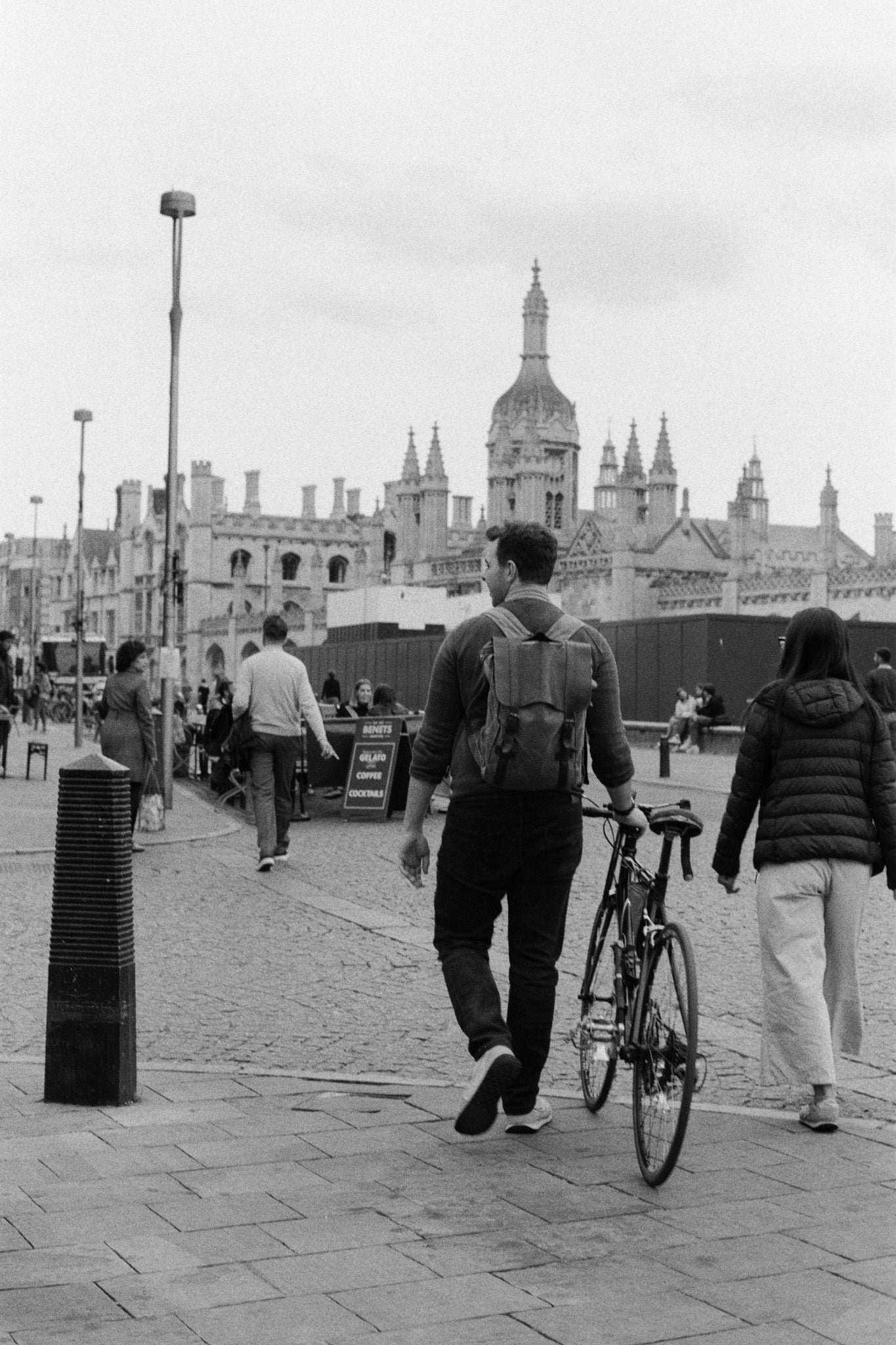 A black and white city buildings on the background and people walking in the street in the foreground.