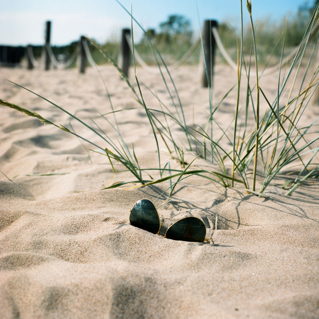 Sun glasses and hay in the beach sand with some poles and ropes on the background.