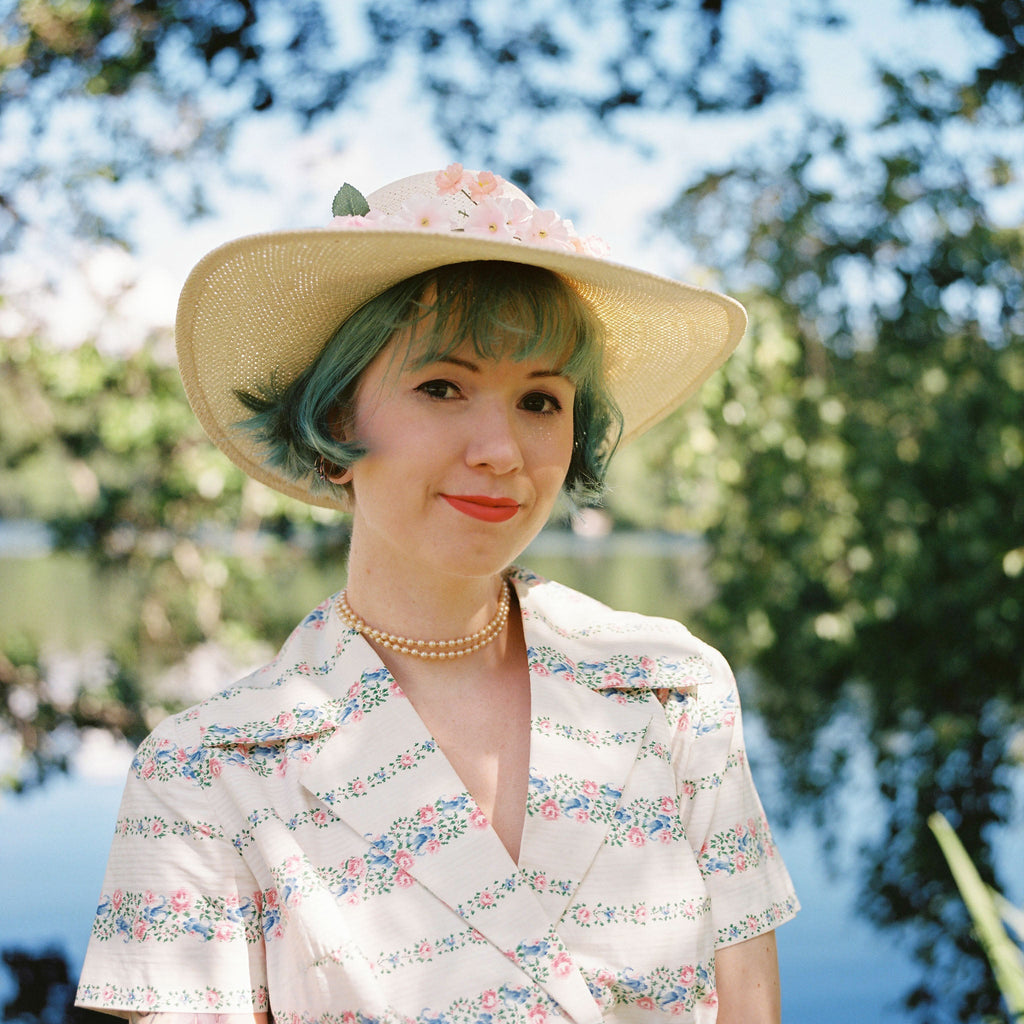 A woman with a hat and some trees and lake on the background.